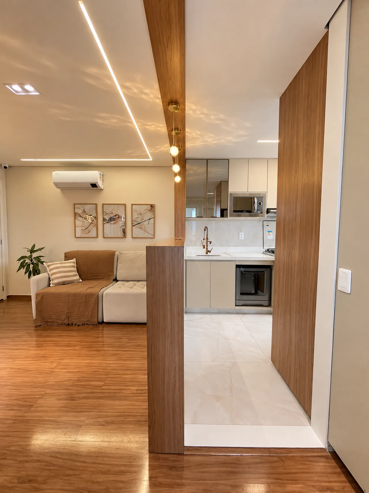 Sala integrada à cozinha com painéis de madeira, iluminação embutida e porcelanato claro em projeto de arquitetura em Belo Horizonte